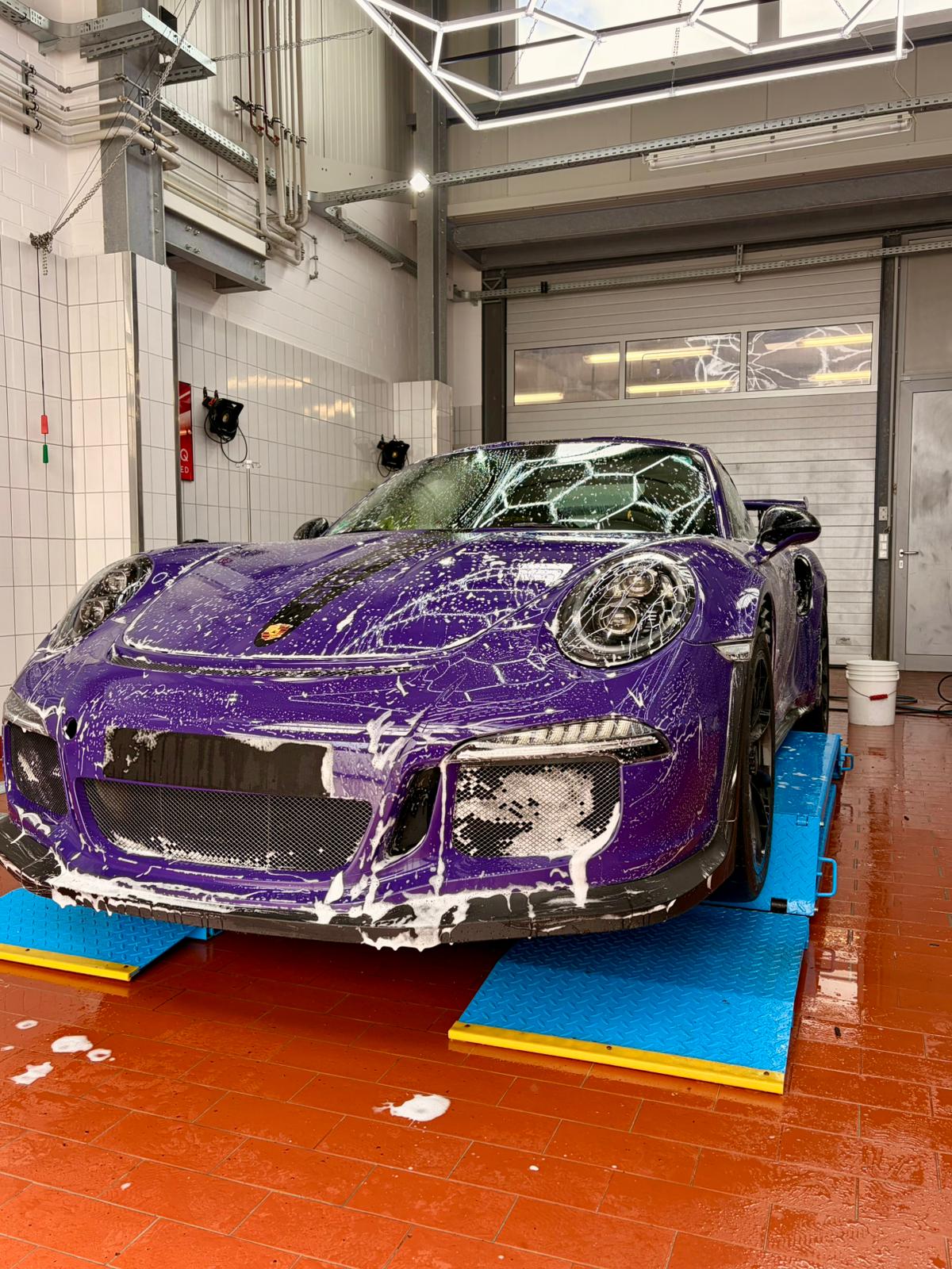 violetter Porsche auf Arbeitsbühne in Werksatt, einshamponiert